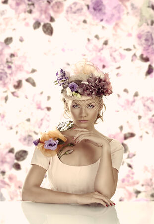 pretty blonde girl with flowers on the hat and on the shoulder, she is in front of the camera, looks in to the lens with left hand under the chinの写真素材