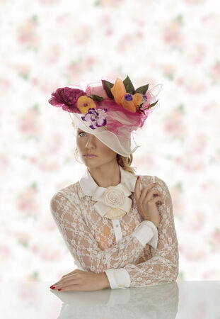 pretty girl behind table with vintage shirt and flowers on the hat, she looks in to the lens and the left eye is covered BY THE HATの写真素材
