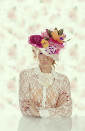 pretty girl behind table with vintage shirt and flowers on the hat, she is in front of the camera and looks in to the lensの写真素材