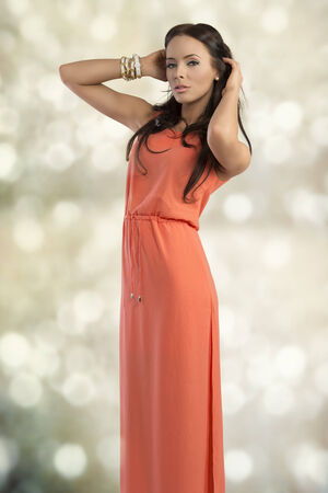 cute female with elegant style and long brown hair, wearing orange dress and bracelets, sensual pose の写真素材