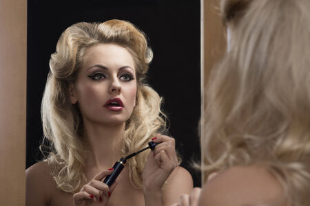 fashion blonde woman with elegant hair-style and make-up applying mascara in front of the mirror の写真素材