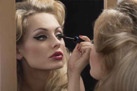 close-up shoot of fashion elegant woman applying mascara in front of the mirror, blonde hair-style の写真素材