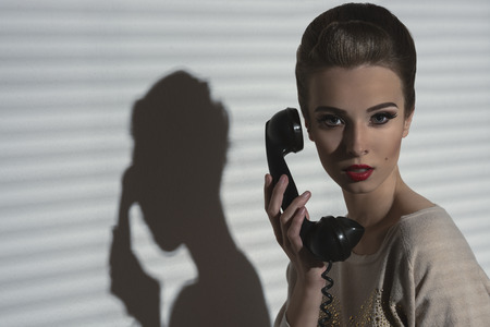charming woman with vintage style and elegant hair-style talking on the retro phone, taking receiver near the face の写真素材