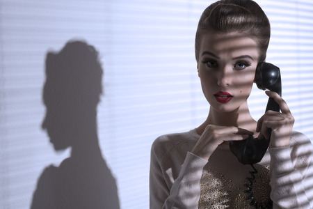 sexy female with elegant hair-style and make-up talking on the phone with vintage receiver の写真素材