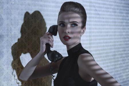 indoor shoot of fashion elegant woman talking on vintage phone with worried expression, indoor half-light atmosphere の写真素材