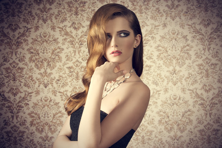 beautiful young girl in fashion pose with long wavy hairdo, stylish necklace, trendy make-up and dark dress の写真素材