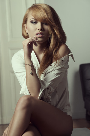 provocative young female wearing only open shirt posing with naked legs and shoulder in erotic poseの写真素材