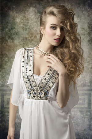creative fashion portrait of beauty woman with antique dress and golden jewellery posing with curly long hair and stylish make-upの写真素材