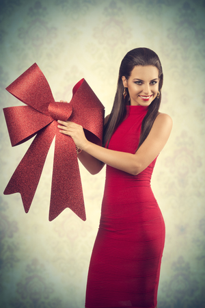 pretty girl with long brown hair  posing in christmas concept shoot with red dress and big red bow, smiling and looking in cameraの写真素材