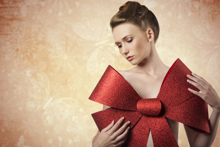 christmas shoot of sensual young girl adorned like a present  with elegant hair-style, colorful make-up and big red glitter bow on her beast,の写真素材