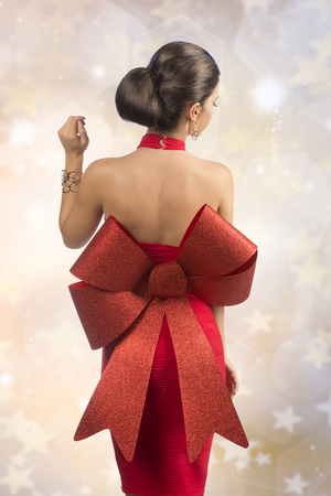 sexy brunette woman posing turned on her back with red christmas dress, big glitter bow and golden jewelleryの写真素材