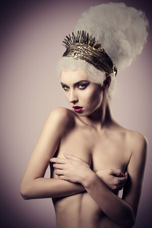 creative fashion shoot of naked woman with baroque artistic hairdo, golden accessories on the head and stylish make-up. Covered her breast and looking in cameraの写真素材