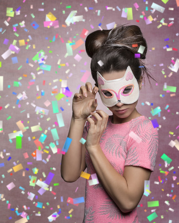 charming brunette girl masquerade with cat mask, in aggressive pose with creative hairdo and stylish pink t-shirtの写真素材