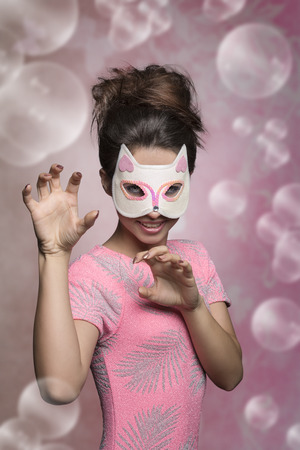 carnival portrait of sexy brunette with kitten mask in cat pose with creative hair-style and stylish pink t-shirt.の写真素材