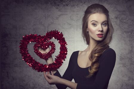 Young, fresh, romantic, pretty valentine girl with nice hairstyle and makeup is holding a heart.の写真素材