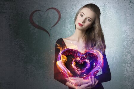 Young, beautiful, romantic valentines girl with curly hairstyle and with valentine heart.She wears black top and brown makeup.の写真素材
