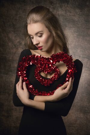 Beautiful, young, elegance, girl with brown nice long hairstyle  and black top is holding heart symbol of love.の写真素材