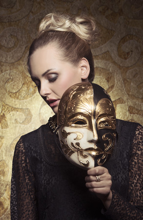 carnival portrait of masquerade blonde woman with antique baroque lady style and venetian mask in the hand. Gothic lace dress and precious jewelleryの写真素材