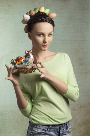 Attractive, brunette, spring woman with funny hairstyle and little basket with easter decorations, She wears green top and jeans.の写真素材