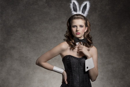 very brunette girl wearing like playgirl with fluffy bunny ears, black papillon and corset posing in glamour easter shootの写真素材