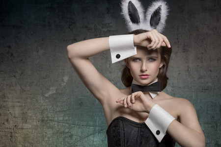 sexy brunette pinup girl with fluffy bunny ears, papillon and dark corset posing in easter glamour...