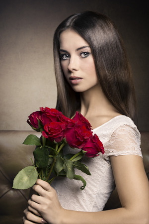 Young, romantic, brunette woman in white dress and bouquet of red roses. she is looking very hypnotizing at cameta.の写真素材