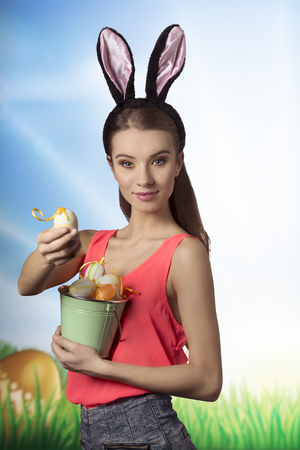 Pretty, easter girl with rabbit, fluffy ears and bucket of easter eggs. She wears to and jeans shorts.の写真素材