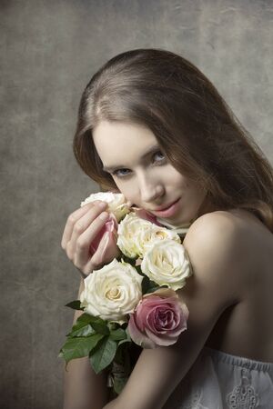 lovely woman with spring style and long hair posing in romantic pose with bouquet of white and pink rosesの写真素材