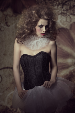 sensual brunette woman wearing like a dancer with sad clown make-up and crazy hair-style. Gothic fashion creative portraitの写真素材