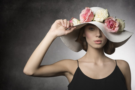fashion summer close-up portrait of sexy brunette girl with black dress and big hat with colorful flowers, romantic spring style. she Looking in cameraの写真素材