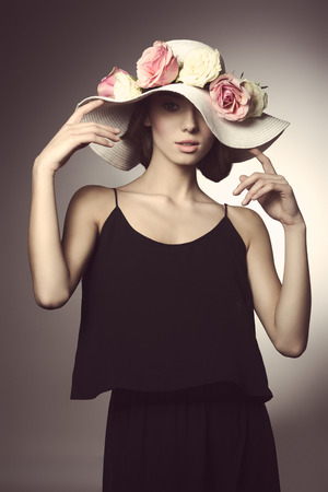 romantic young woman with black dress and big elegant hat with colorful flowers. Looking in camera in fashion poseの写真素材