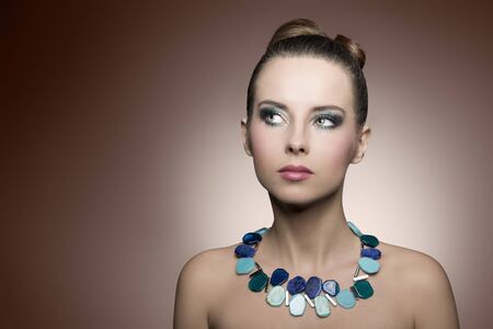 close-up portrait of beautiful brunette girl with summer turquoise make-up and stylish necklace. Creative modern hair-styleの写真素材