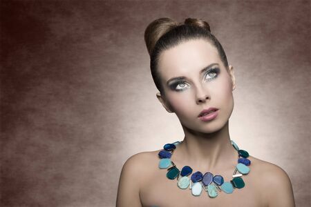 close-up beauty shoot of cute brunette woman with creative hair-style and summer turquoise make-up. Stylish necklace and surprised expressionの写真素材
