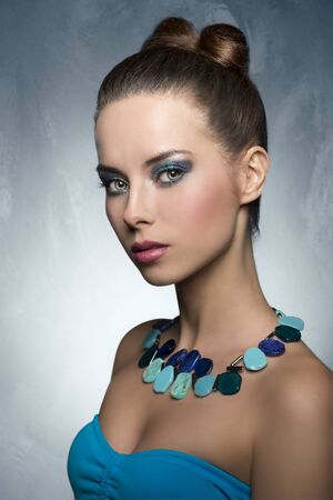 cute brunette female with funny summer hair-style and turquoise make-up, Wearing stylish necklace and looking in camera with charming expressionの写真素材