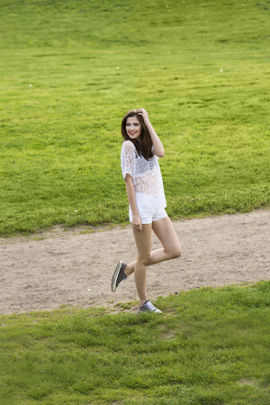 Casual fashion girl , near a green grass , outside in the park wearing a white shirt and short she is looking on one side smilingの写真素材