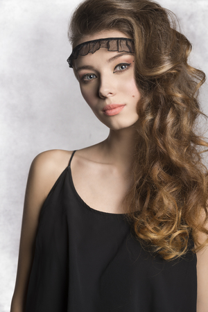 pretty brunette girl with long wavy shiny hair and stylish make-up wearing black summer dress and looking in cameraの写真素材