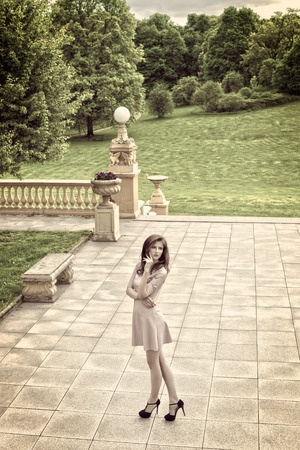 hdr color virage , outside fashion portrait of elegant girl with pink dress and black heels posing in terrace of old building near a green gardenの写真素材