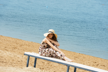 romantic cute woman , sitting in the beach , she is wearing floral dress hat , she enjoy the sun in the beautiful day, she is restingの写真素材