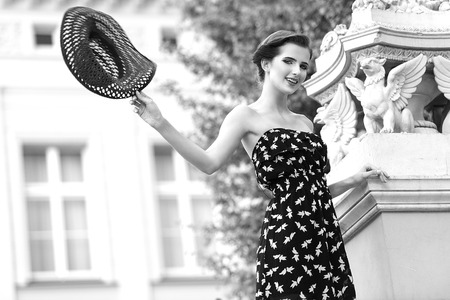black and white Elegant pretty woman , wearing a blue summer dress , she flying an hat in act to say hello . looking in camera.の写真素材
