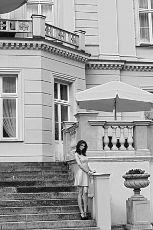 pink dressed nice girl , standing outside stairs of an old fashion bulding . she is looking in camera. in black and white shotの写真素材