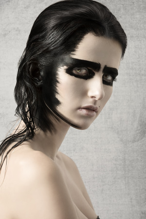 beauty shoot of pretty young girl with strong black painted make-up on her visage and on hair. Looking in camera with charming eyesの写真素材