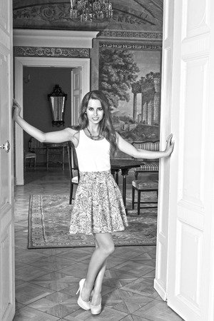 pretty brunette girl posing in indoor portrait in the room of ancient palace with elegant skirt, golden necklace and heels, smiling and looking in camera , black and whiteの写真素材