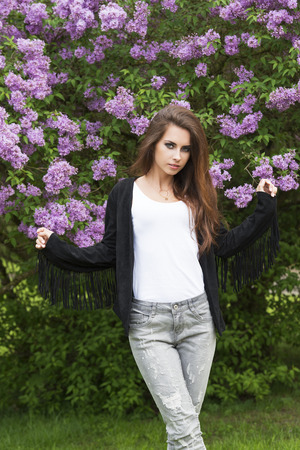 cute woman posing outdoor in fashion portrait in the garden near flowered bush, wearing cute leather jacket and jeans, rock make-up looking in cameraの写真素材