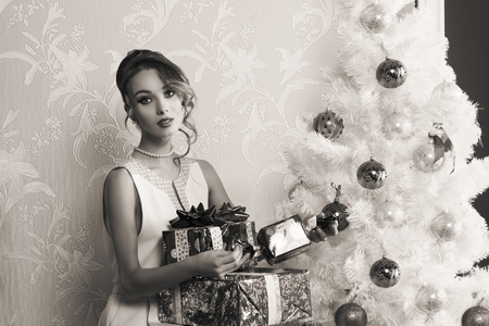 black and white christmas portrait of stunning elegant fashion girl with some gift boxes near decorated xmas treeの写真素材