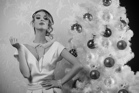 BW image of stunning woman with aristocratic fashion style and pose near decorated christmas tree with elegant clothes, precious pearl necklace and stylish make-upの写真素材