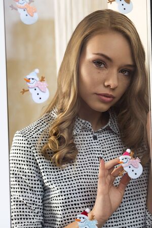 stunning young woman with freckles, fashion shirt and natural make-up posing in christmas portrait trough window decorated by funny xmas stickersの写真素材