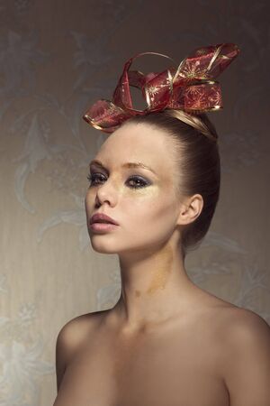 beauty christmas portrait of cute woman with freckles, shiny golden make-up and creative hairdo with red ribbon. naked shouldersの写真素材
