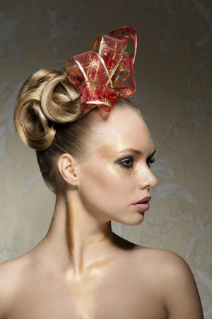 pretty girl with perfect skin with freckles posing turned on profile with creative glossy christmas make-up and red ribbon in elegant hair-styleの写真素材