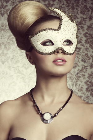 Stunning blonde lady with elegant hair-style and romantic eyes posing with decorated mask on her visage and stylish necklace.の写真素材