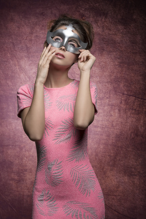 charming girl with sexy pink dress and hair-style posing with silver mask and romantic expressionの写真素材